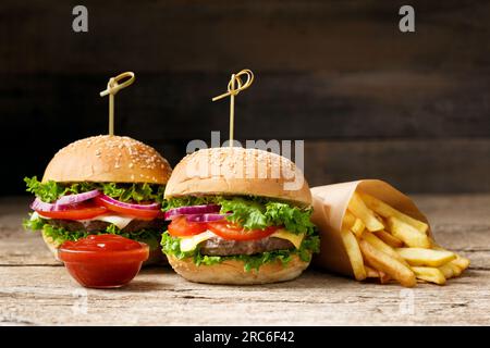 Succulento e appetitoso hamburger di manzo, patatine fritte, due salse su un tavolo di legno. Fast food americano, hamburger fatto in casa. Foto Stock