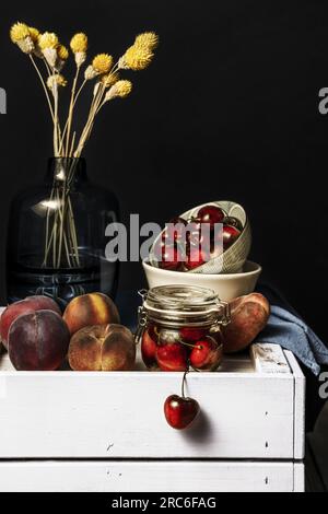 Una natura morta con frutta matura su una scatola di legno dipinta e un vaso di vetro con fiori secchi Foto Stock
