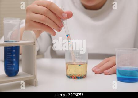 Ragazza che mescola liquidi colorati al tavolo bianco in interni, primo piano. Set di esperimenti chimici per bambini Foto Stock