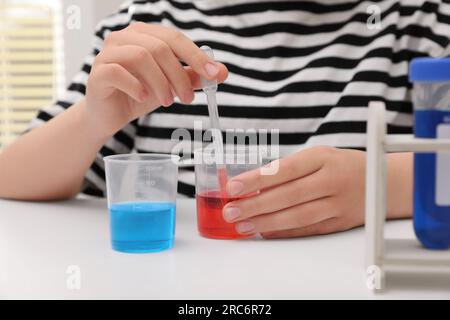 Ragazza che mescola liquidi colorati al tavolo bianco in interni, primo piano. Set di esperimenti chimici per bambini Foto Stock