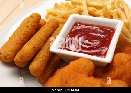 Gustoso ketchup, patatine fritte, pepite di pollo e bastoncini di formaggio sul piatto, primo piano Foto Stock