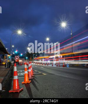 Coni stradali arancioni che fiancheggiano la strada. Percorsi leggeri degli autobus che si avvicinano all'incrocio. Lavori stradali ad Auckland. Formato verticale. Foto Stock