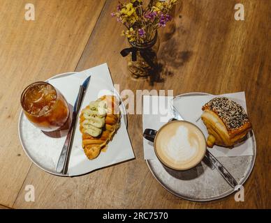 Due caffè, squisiti pasticcini sopra un tavolo di legno. Colazione mattutina con croissant al pistacchio in una caffetteria Foto Stock