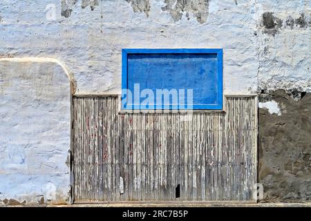 Lanzarote, Isole Canarie, Arrecife, fronte mare, muro lavato in bianco battuto con vernice che peeling pannello di legno a doghe e finestra blu Foto Stock