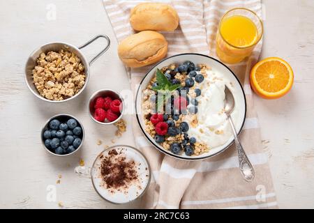 Muesli con yogurt e frutti di bosco per una sana colazione. Ciotola di yogurt greco con muesli, mirtilli e lamponi su sfondo bianco, vista dall'alto. Foto Stock