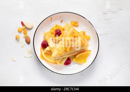 Tradizionale suzette di crepe francese con salsa d'arancia in un piatto bianco su sfondo bianco. Vista dall'alto. Foto Stock
