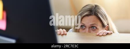 Donna spaventata e scioccata nel panico dietro la scrivania guardando lo schermo del computer. Foto Stock