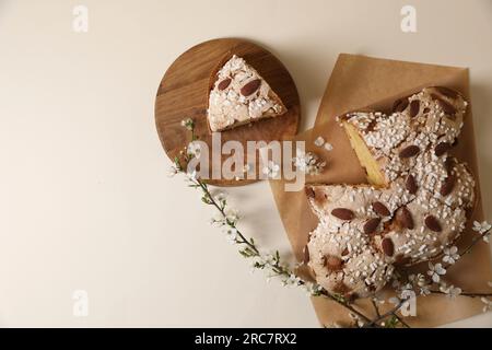 Delizioso dolce pasquale italiano tagliato (colomba di Pasqua tradizionale) e rami fioriti su tavolo beige, piatto. Spazio per il testo Foto Stock