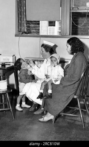 New York, New York: c. 1933. Un'infermiera della scuola pubblica controlla la gola di un bambino, la cui madre e fratello sono presenti. Foto Stock