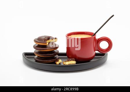 Tazza di caffè espresso rosso ripiena di caffè forte e biscotti su un piatto nero isolato su fondo bianco Foto Stock