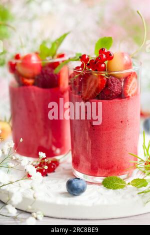 Mousse al gusto di frutti di bosco condita con frutti di bosco freschi in bicchieri. Dessert estivo con fragole, lamponi, ribes rosso, ciliegia e mirtillo Foto Stock