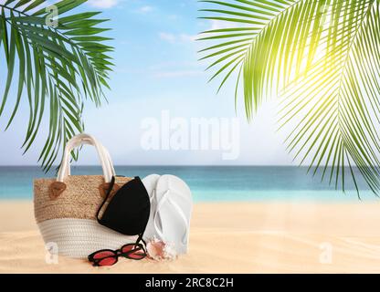 Borsa con zona bikini e accessori sulla soleggiata spiaggia dell'oceano, spazio per messaggi. Vacanze estive Foto Stock