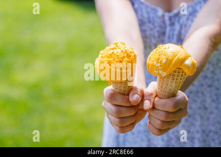 Le mani delle donne tengono un gelato rinfrescante in coni di waffle con un pizzico di saporito sapore di limone. Con spazio di copia Foto Stock