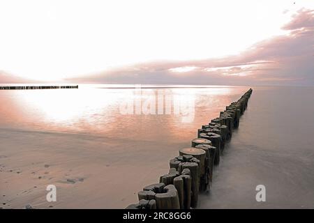 Frangiflutti di legno sulla spiaggia al tramonto. Mar Baltico. Foto Stock