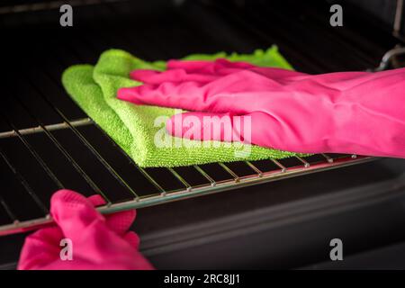 Pulizia del forno. La mano di una donna con guanti rosa pulisce il forno all'interno. Forno pulito in cucina. Foto Stock