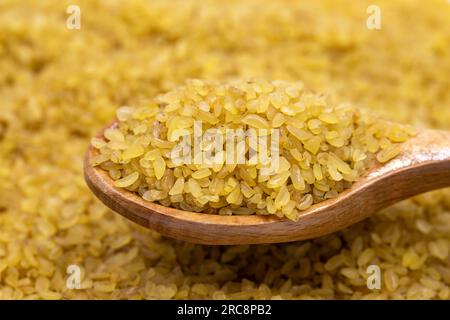 Grano bulgur crudo su cucchiaio di legno, legumi come sfondo. ravvicinare il grano bulgur secco crudo Foto Stock
