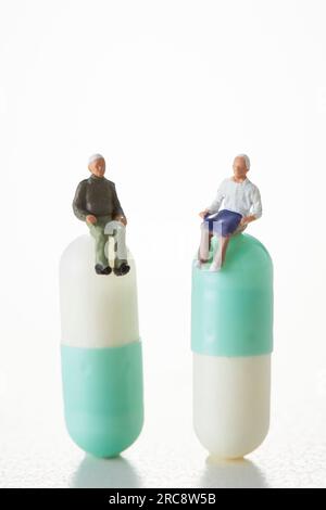 Due anziani in miniatura seduti su pillole a capsula Foto Stock