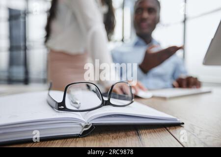 Gli occhiali sono sul tavolo da lavoro. Su uno sfondo sfocato, il ragazzo lavora con un notebook e prende appunti in un notebook. Foto Stock