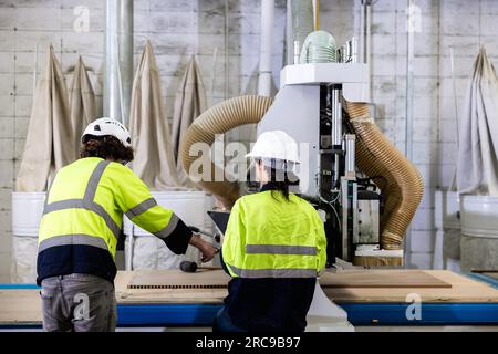 il controllo del lavoro di squadra aziona la fresatrice del legno nelle officine di mobili in legno. il personale tecnico lavora in team con macchine moderne del settore Foto Stock