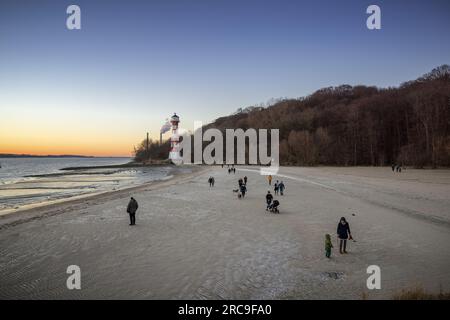 Eisiger Winternachmittag am Strand von Wittenbergen ad Amburgo-Rissen. Die untergehende Sonne beleuchtet den Leuchtturm. Im Hintergrund die Schornstei Foto Stock