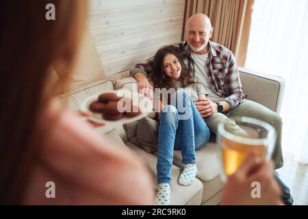 Donna che serve biscotti e tè alla famiglia nel soggiorno Foto Stock