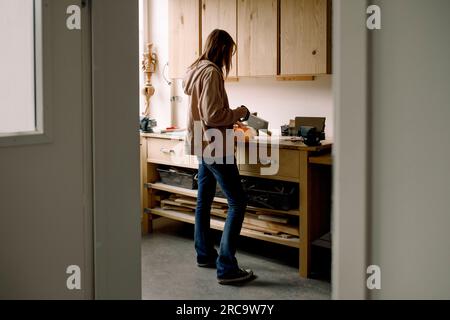 Studentessa adolescente che taglia legno durante la lezione di carpenteria visto attraverso la porta Foto Stock