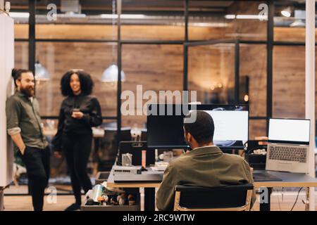 Vista posteriore di un uomo d'affari seduto con un computer che guarda i colleghi in ufficio Foto Stock