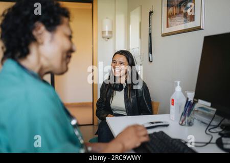 Giovane donna felice seduta da una dottoressa alla scrivania della clinica Foto Stock