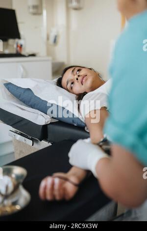 Giovane donna sdraiata sul tavolo da esame mentre il chirurgo opera in ospedale Foto Stock