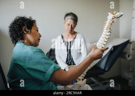 Medico che spiega il paziente anziano sul modello della colonna vertebrale in clinica Foto Stock