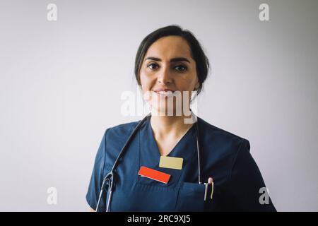 Ritratto di una donna sorridente operatrice sanitaria contro il muro bianco Foto Stock