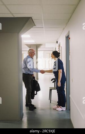 Infermiera donna che fa stretta di mano con il paziente anziano maschile mentre si trova in corridoio all'ospedale Foto Stock