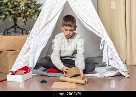 Un bambino, un ragazzo adolescente, avvolge i regali, fa origami da carta artigianale per una vacanza a casa. Regali con le tue mani. Fatelo da soli. Foto Stock