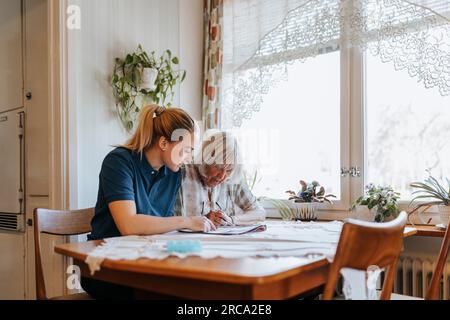 Infermiera femminile che aiuta una donna anziana a fare puzzle a casa Foto Stock