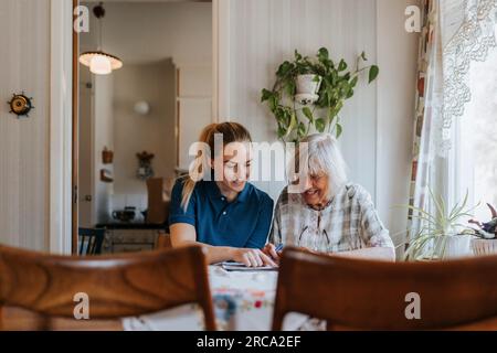 Infermiera sorridente che assiste la donna anziana a fare puzzle a casa Foto Stock