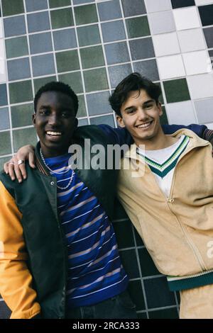 Ritratto di amici maschi sorridenti in piedi con le braccia intorno a un muro piastrellato Foto Stock