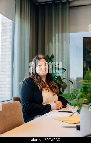 Ritratto di sorridere imprenditrice seduto alla scrivania in ufficio Foto Stock