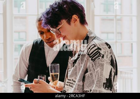 Sorridente persona non binaria che condivide lo smartphone con un collega durante l'evento al centro congressi Foto Stock