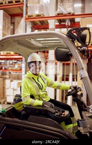 Ritratto di una giovane lavoratrice sorridente che guida carrelli elevatori nell'industria Foto Stock