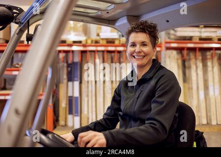 Ritratto di una donna sorridente che guida un carrello elevatore a forche nell'industria del legname Foto Stock