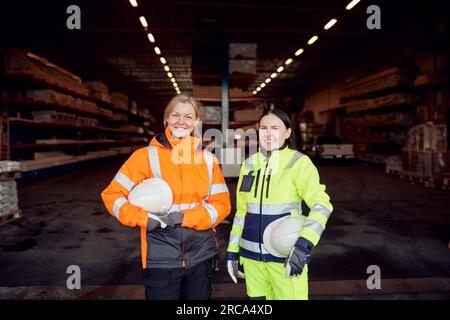 Ritratto di donne sorridenti che indossano indumenti da lavoro protettivi in un magazzino di distribuzione Foto Stock