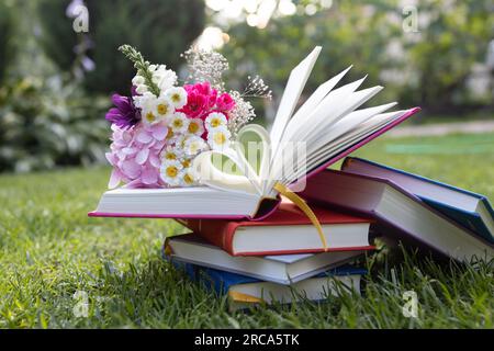 diversi libri multicolori giacciono sull'erba. libro aperto, le cui pagine sono piegate a forma di cuore, bouquet di fiori su di esso. concetto di lettura, educato Foto Stock