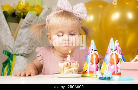 Una bambina di due anni fa spara una candela su una torta di compleanno, fa un desiderio Foto Stock