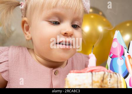 Una bambina di due anni fa spara una candela su una torta di compleanno, fa un desiderio Foto Stock