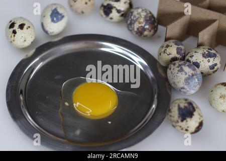 Uovo di quaglia incrinato. Tuorlo d'uovo dal guscio dell'uovo di quaglia. Queste uova sono di piccole dimensioni e hanno conchiglie color crema con splotch marroni e giallo intenso Foto Stock