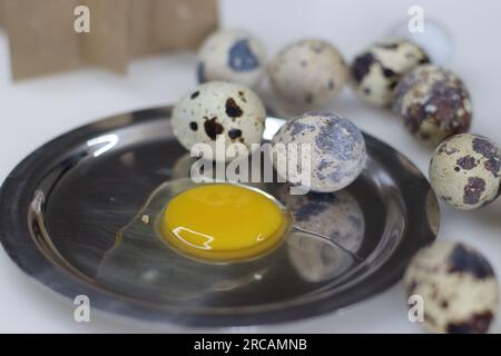 Uovo di quaglia incrinato. Tuorlo d'uovo dal guscio dell'uovo di quaglia. Queste uova sono di piccole dimensioni e hanno conchiglie color crema con splotch marroni e giallo intenso Foto Stock