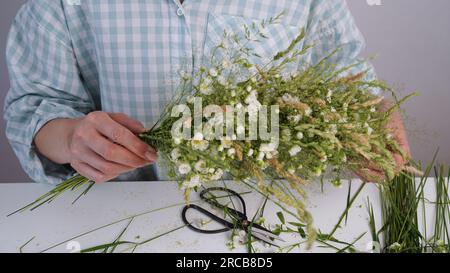 Master class floristica sulla corona di fiori per la festa di Ivan Kupala. La donna trita una corona di erbe e fiori freschi, simbolo pagano, solstizio da Foto Stock