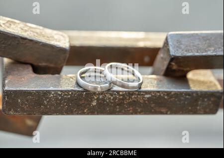 Due mani con anelli nuziali poggiano su una robusta catena di ancoraggio. Foto Stock