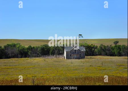 Una casa in pietra deserta si trova sulla prateria aperta del Kansas. La fattoria e' a due piani e in legno. La vernice bianca è incrinata e si stacca,. Foto Stock