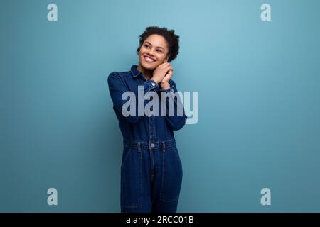 giovane donna in brunetta ispanica con morbidi capelli ricci in tuta di denim blu Foto Stock